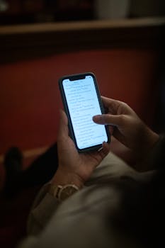 A person holding and looking at a smartphone screen in a dim-lit indoor setting.