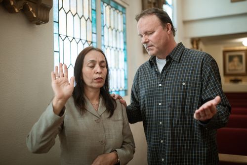 Free A man and woman praying together inside a church with stained glass windows. Stock Photo