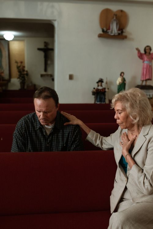 Free A senior woman comforts a man in deep prayer at a church. Stock Photo