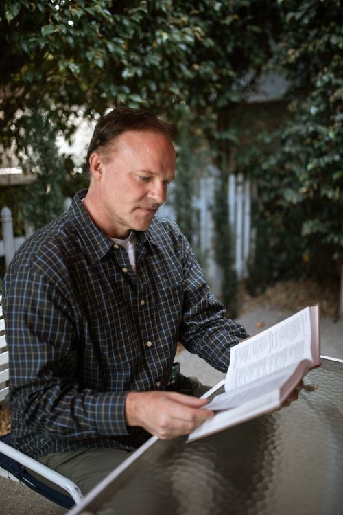 Free Adult man reading a Bible outdoors in a serene garden setting. Stock Photo