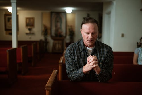 Man in Black and White Plaid Dress Shirt Praying on Church