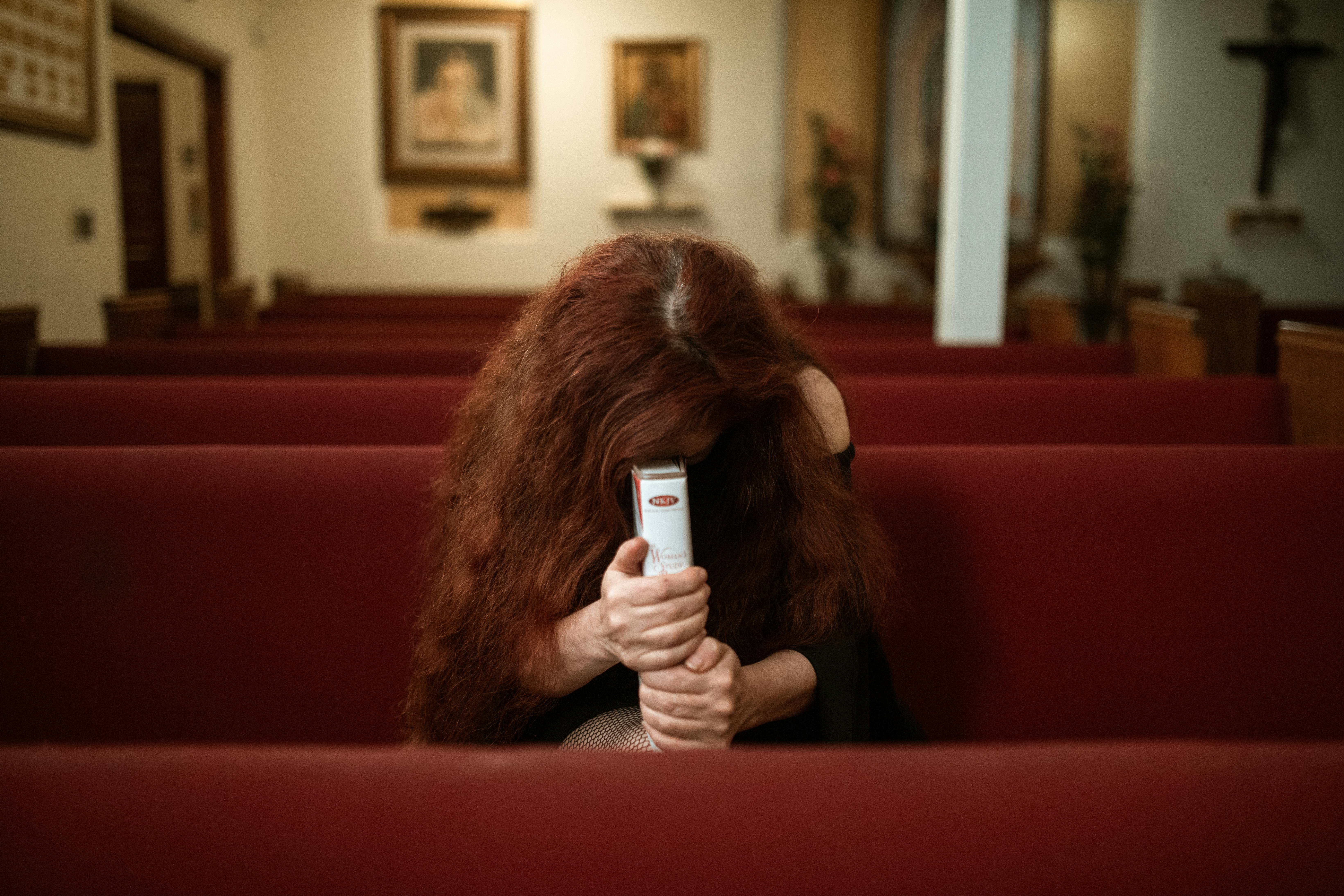 a woman in black long sleeve shirt sitting on red bench while praying