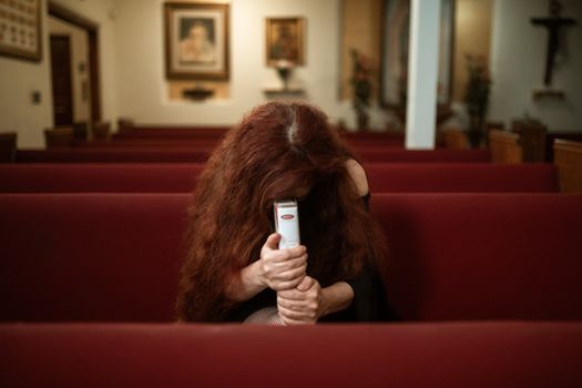 A Woman in Black Long Sleeve Shirt Sitting on Red Bench while Praying