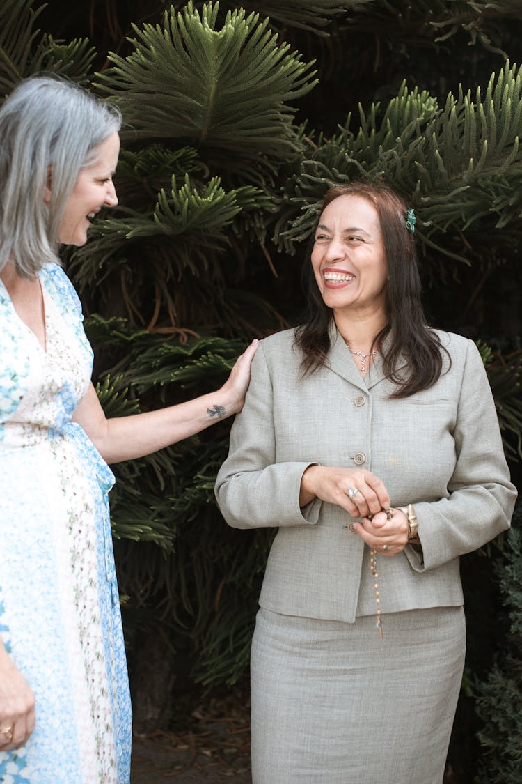 Woman In Floral Dress Standing Beside A Woman In Gray Skirt Suit