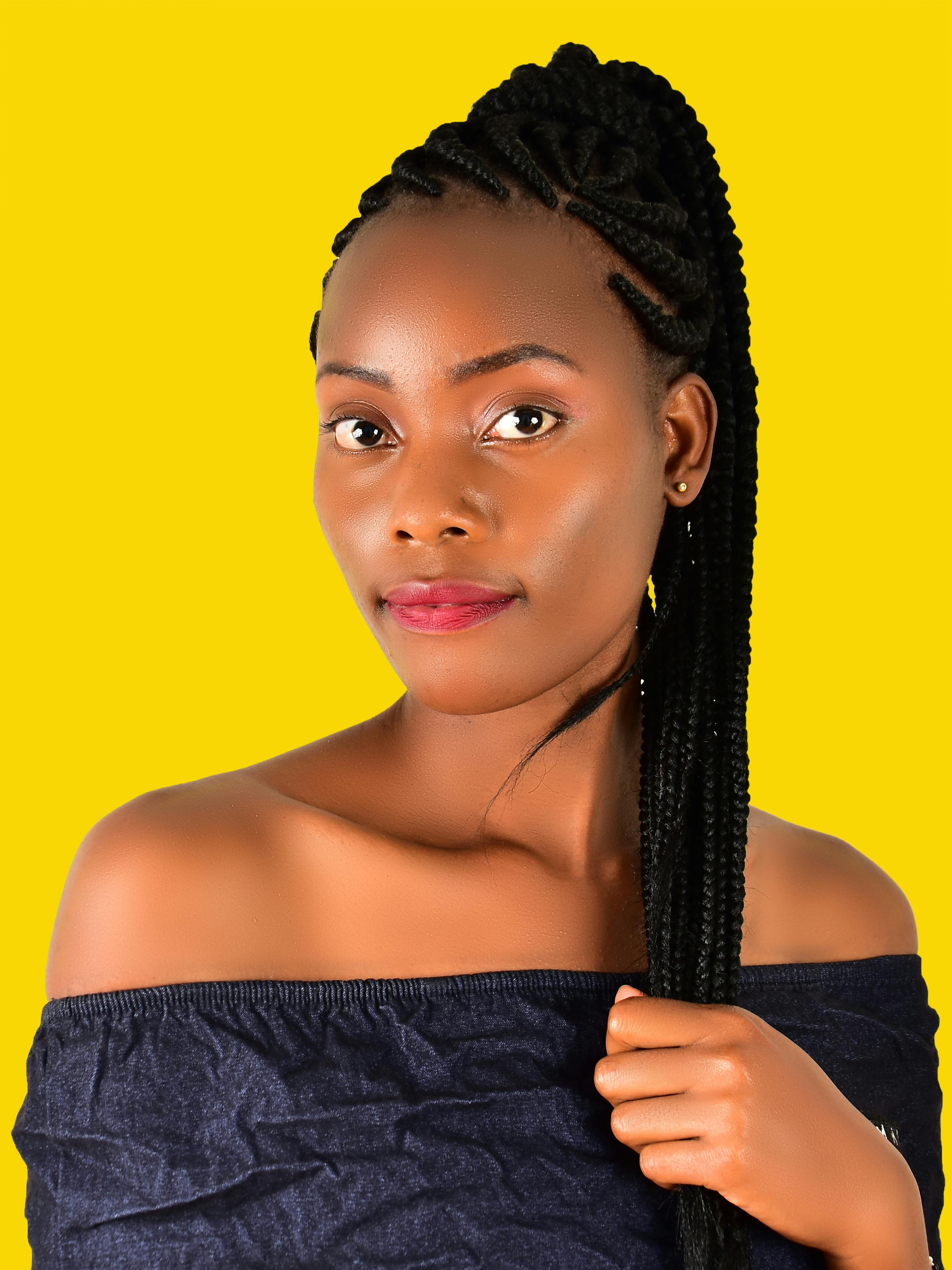 Portrait of a woman in off-shoulder blouse with braided hair against a yellow background.