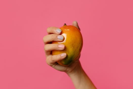 Close-up of a hand holding a ripe mango with a pink background. Vibrant and colorful composition.