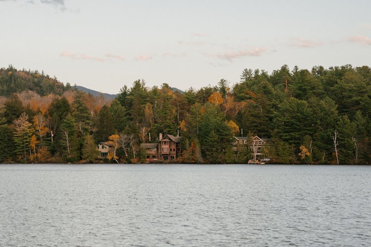 Traditional Cottages In Autumn Forest On Lake Shore