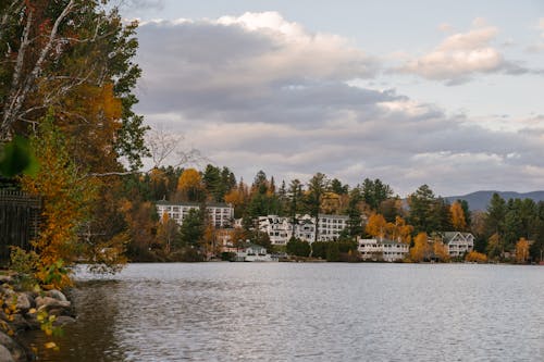 Houses surrounded by lush autumn trees on lake shore at sundown