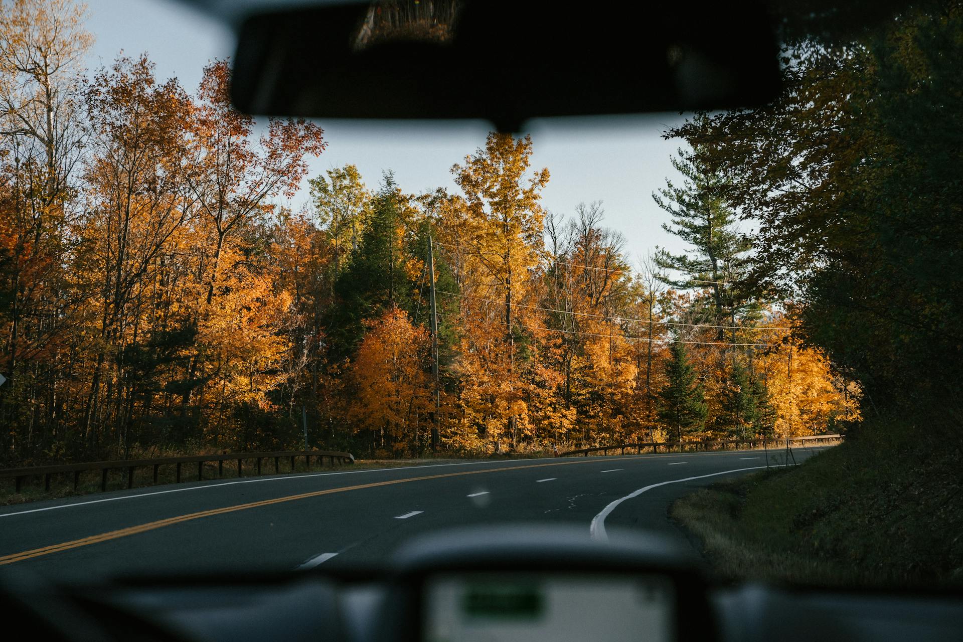 Modern car driving along curvy asphalt road amidst lush autumn trees in countryside on sunny day