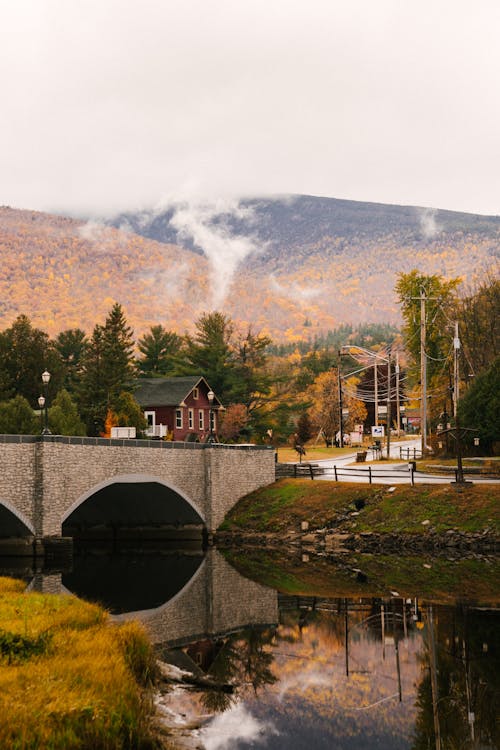 Clouds over mountains and trees with bridge above river in town