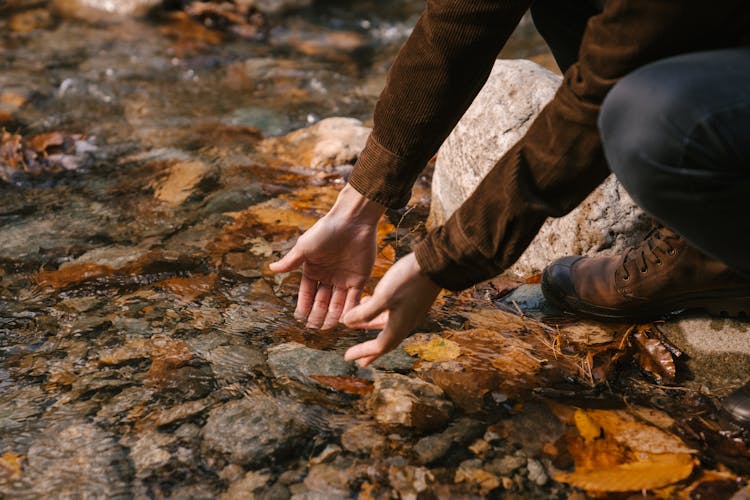 Man Putting Hands In Clear Water Of River