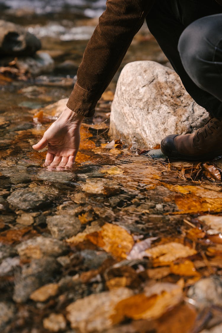 Man On Hunkers On Stony Coast Of Lake