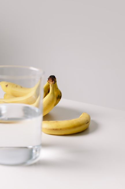 A simple composition with ripe bananas and a glass of water on a white surface.