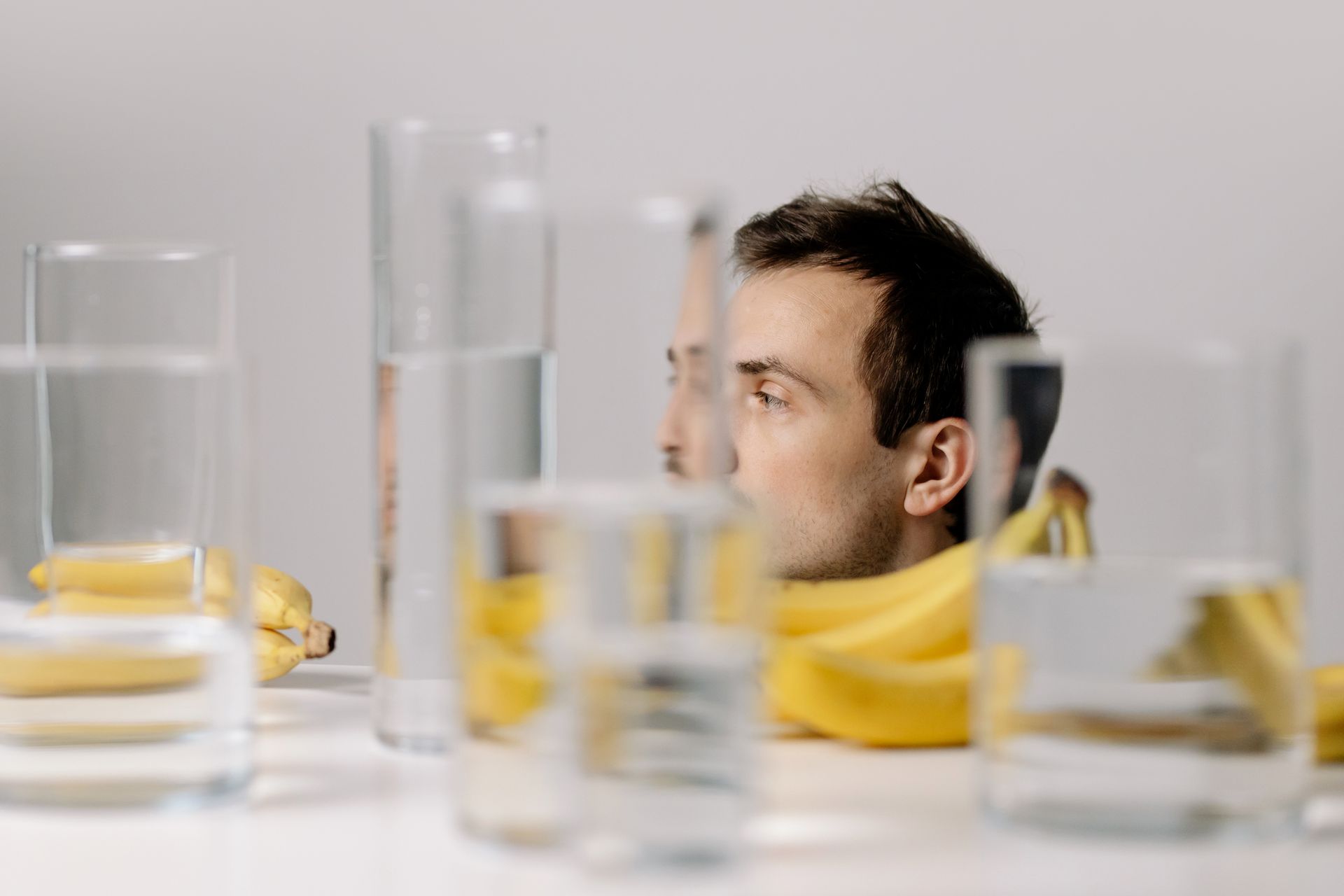 Drinking Glasses with Water Beside Bananas and Man's Head