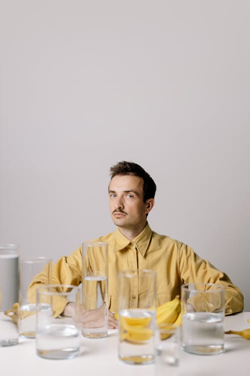 Man in Yellow Dress Shirt Sitting Behind Clear Glasses with Water