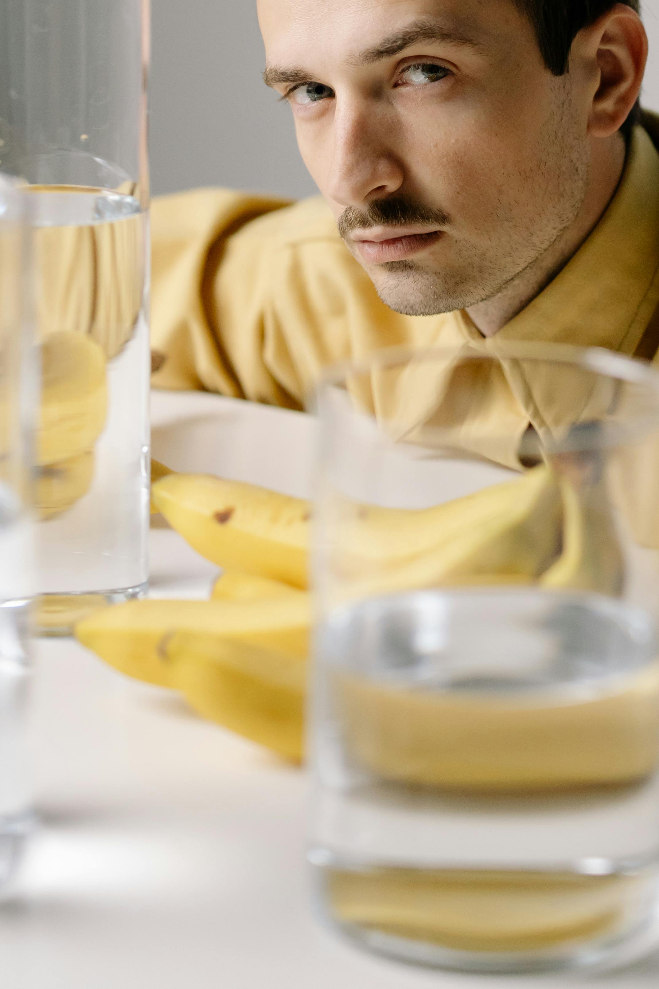 Portrait of a man in a yellow shirt with bananas on a table, captured in a reflective setting.