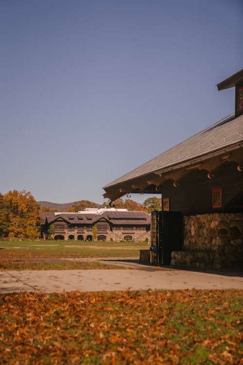 Exterior of old stone building with roof located on backyard on grassy lawn with fallen leaves in autumn day in countryside