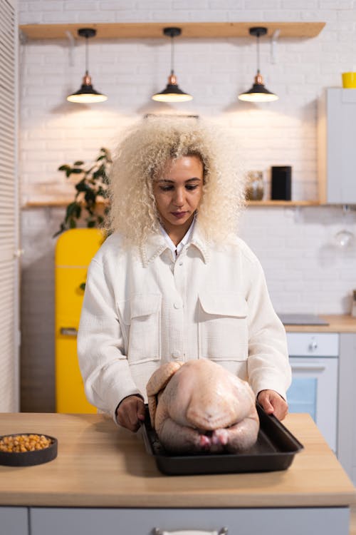 Concentrated female cook standing at table with whole raw turkey on tray while cooking dinner in kitchen at home