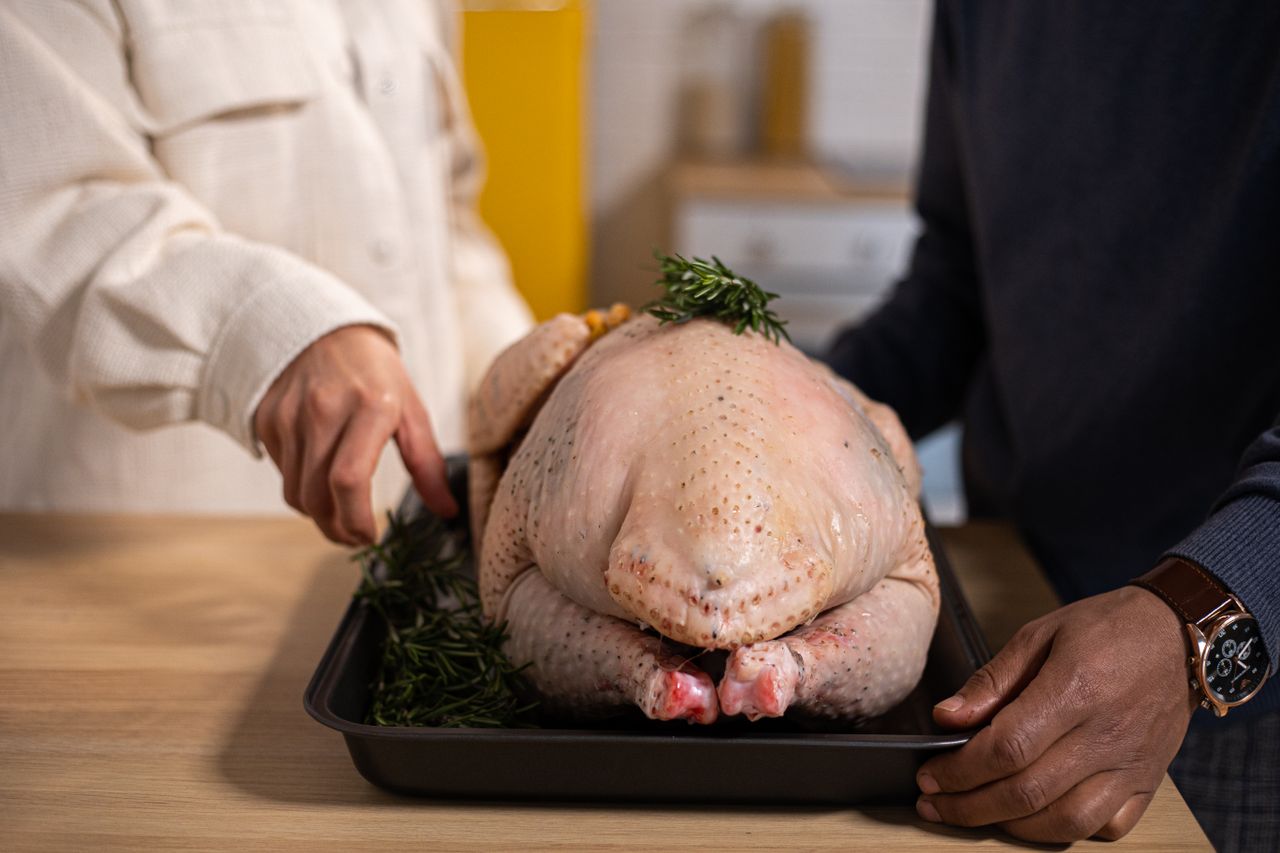 Two people preparing a raw whole turkey with rosemary on a tray