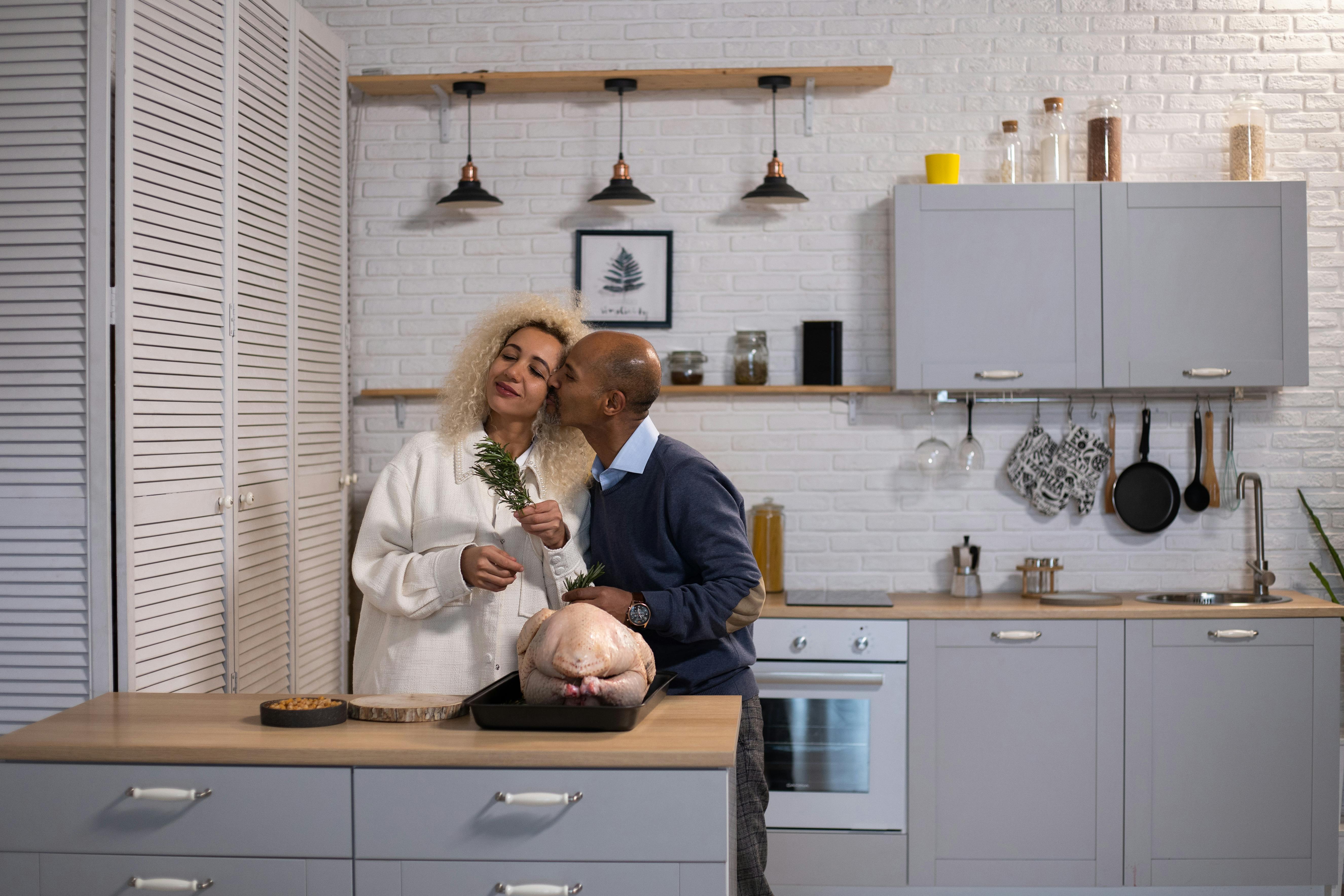 loving black man kissing woman in kitchen with turkey