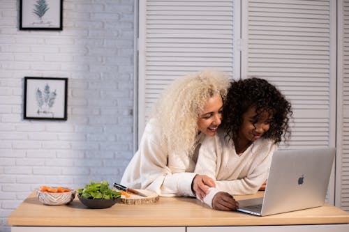 Free Smiling black mother and daughter browsing laptop at kitchen counter Stock Photo