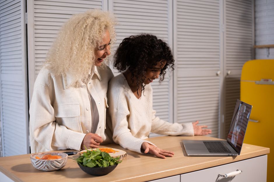 How Food Processors Like Cuisinart 14 Cup Compare to Breville Sous Chef for Meal Prep Side view of happy African American woman and girl having video call on modern laptop at wooden table with food in kitchen