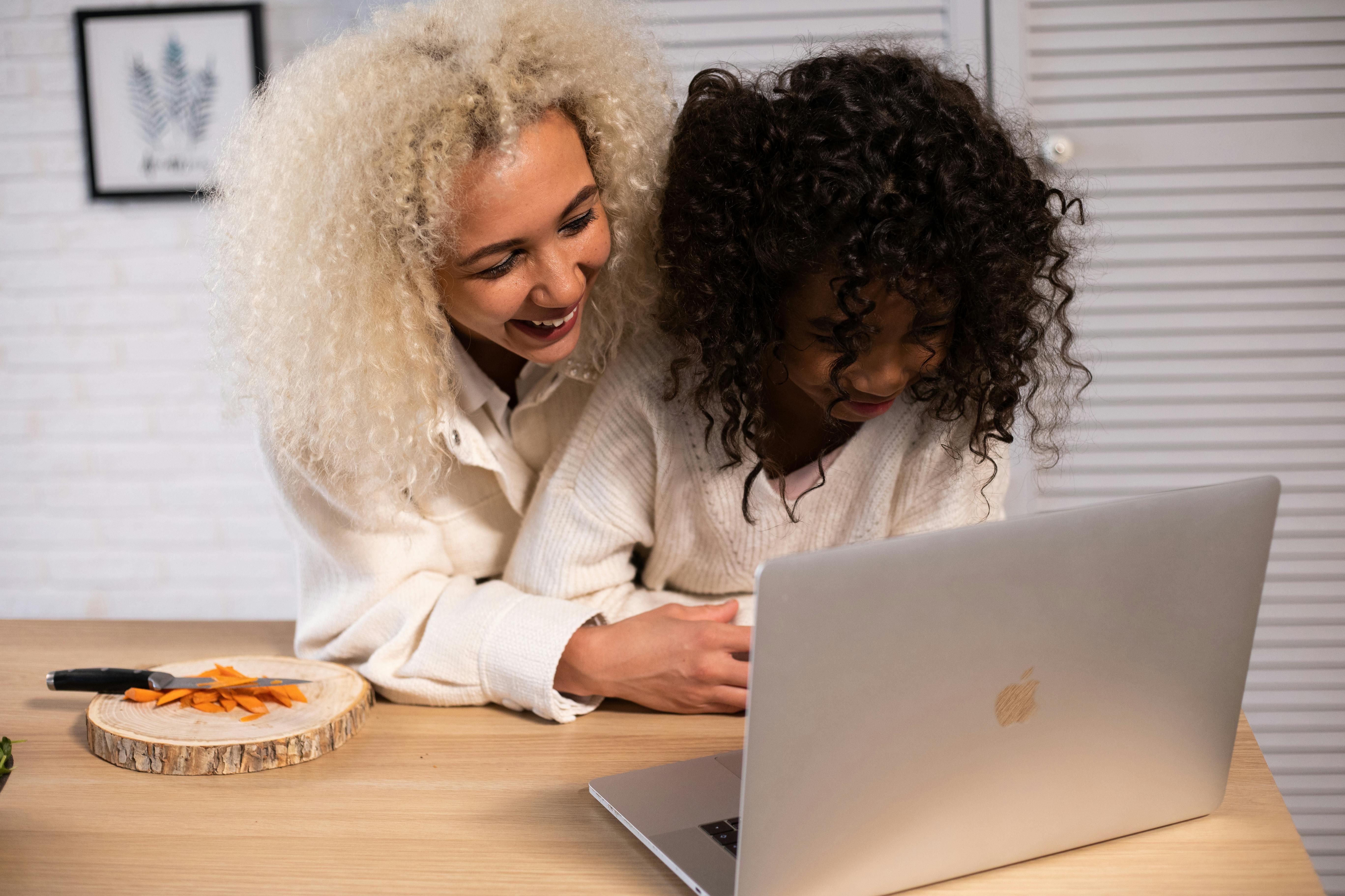 laughing black mother and daughter browsing modern laptop in kitchen