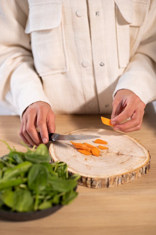 Crop person cutting carrot in kitchen