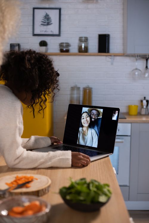Free Side view of anonymous African American kid making video call on netbook while standing at wooden counter with food in kitchen Stock Photo
