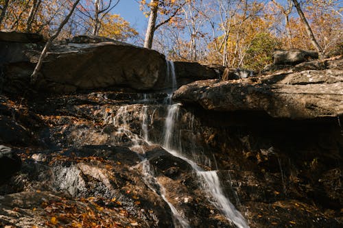 Fast waterfall flowing through heavy rocks in autumn forest under bright clear blue sky