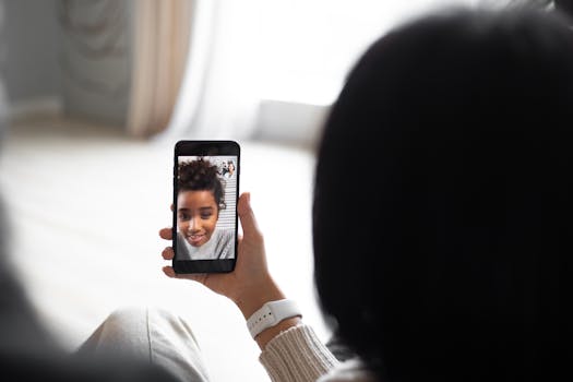 Woman making a video call using smartphone at home, focusing on the screen showing child's face.
