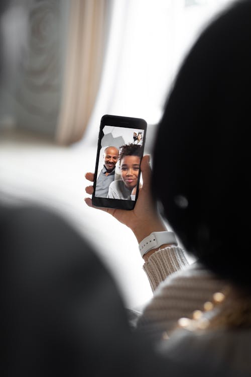 Back view of anonymous female having video chat with black man and girl in light room on blurred background at home