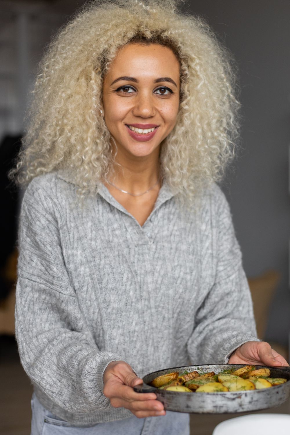 Smiling woman holding a tray of roasted vegetables in a bright kitchen