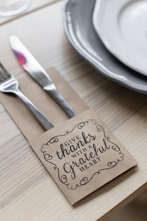 Free From above of metal shiny fork and knife placed in paper cover with inscription for Thanksgiving near plates on wooden table Stock Photo