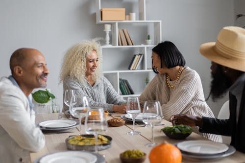 Cheerful multiracial people sitting at wooden table served with vegetarian food and talking to each other while having dinner together