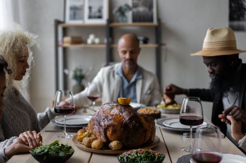 Free Calm multiethnic people sitting at table holding hands with eyes closed while praying before eating dishes for celebrating Thanksgiving Day Stock Photo