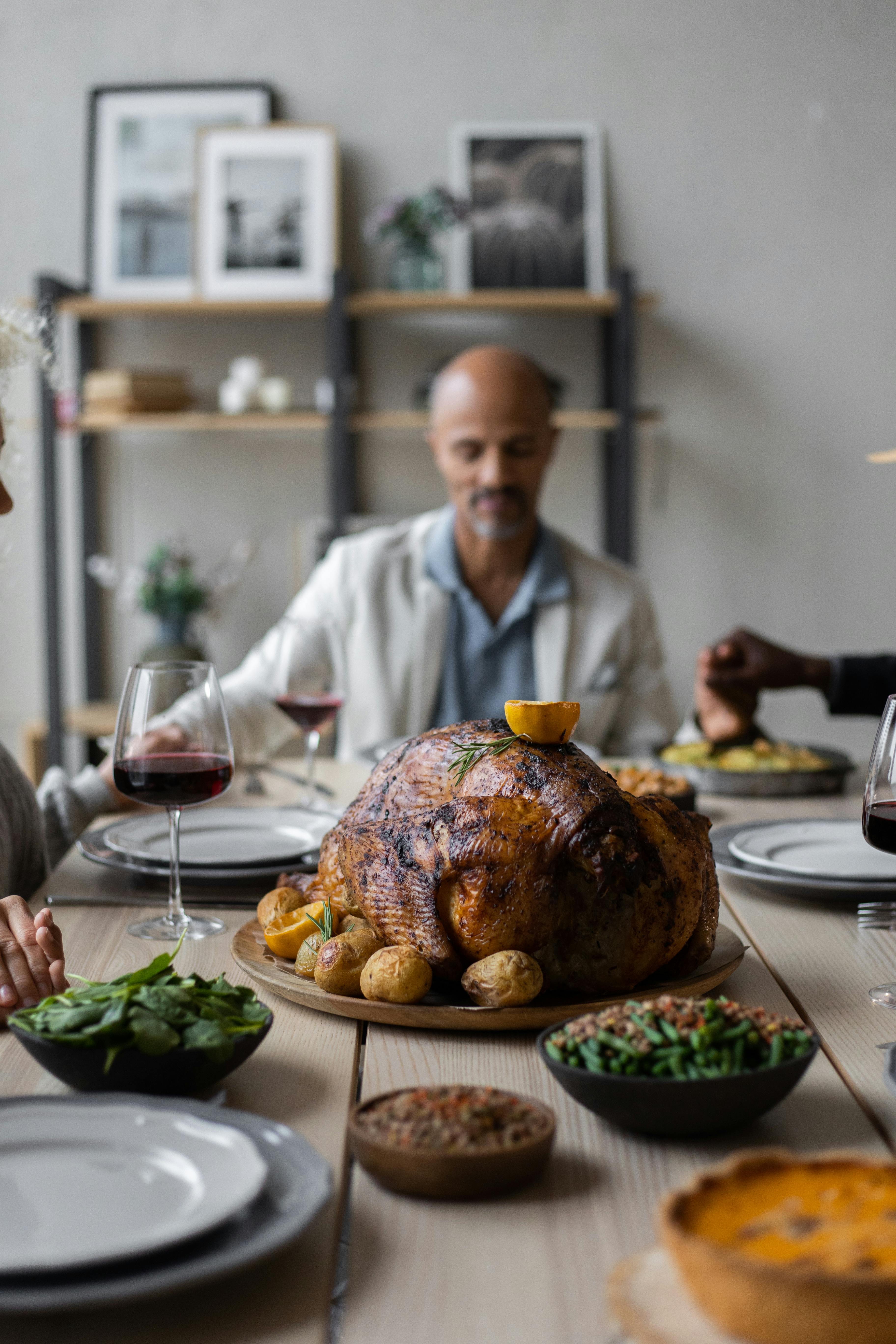 Tranquil diverse people praying together with closed eyes holding hands sitting at table served with dishes for celebrating Thanksgiving Day