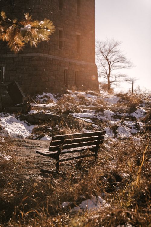 Free Through glass of empty wooden bench near stone structure in countryside area with grass and snow Stock Photo