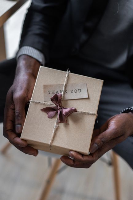 From above of crop unrecognizable African American female with carton gift box decorated with bow and small card with printed inscription