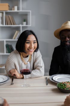 Cheerful diverse couple sitting at wooden table and speaking with guests while having dinner with guests