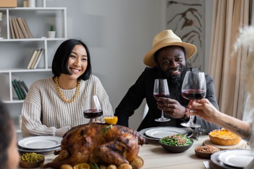 Free Smiling diverse couple sitting at table served with delicious dishes while having dinner on Thanksgiving Day and drinking wine with guests Stock Photo