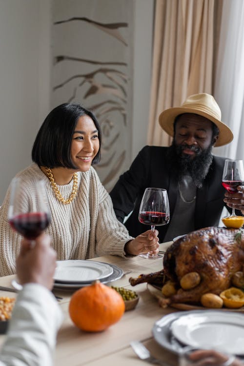 Delighted multiracial couple drinking wine with guests