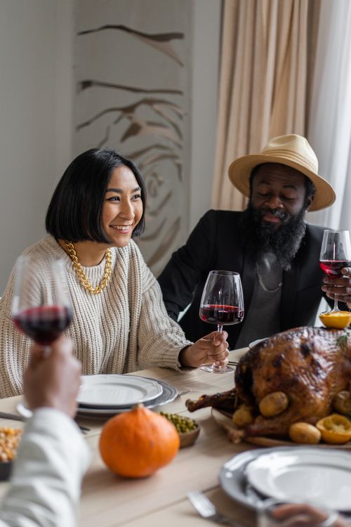 Free Cheerful diverse couple having dinner with guests sitting at table with roasted turkey and drinking wine Stock Photo