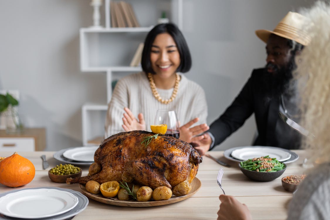 Free Cheerful multiethnic people having dinner together at table with roasted turkey while celebrating Thanksgiving Day Stock Photo