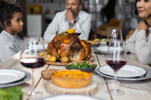 Free Crop multiethnic people sitting at wooden table served with wine and roasted turkey while having dinner on Thanksgiving Stock Photo