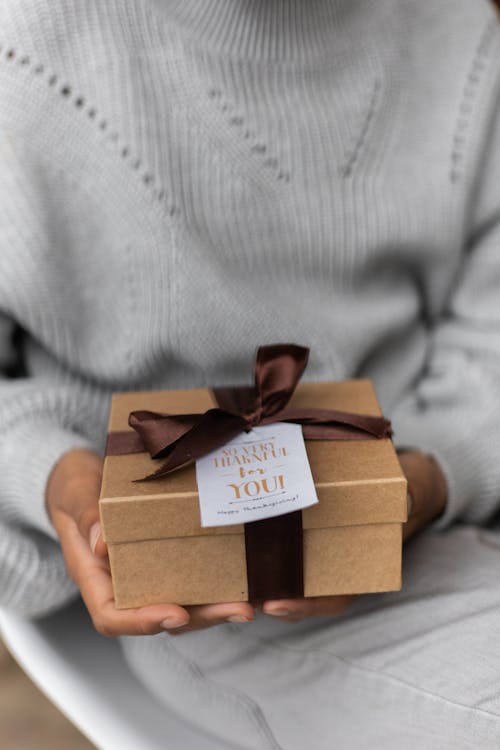 Crop unrecognizable female in knitted sweater with carton present box with bow and small postcard