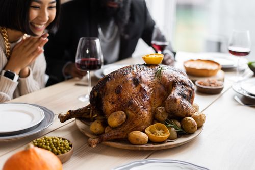 Free From above of positive diverse couple sitting at table served with big roasted turkey and other dishes while celebrating Thanksgiving Day Stock Photo