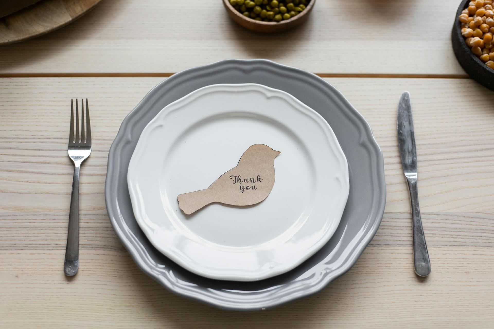Top view of carton postcard cutout in shape of bird with printed Thank You inscription placed on plate on Thanksgiving dinner