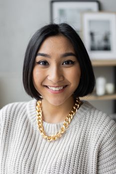 这是一幅室内肖像，画中是一位开朗的年轻女子，她戴着金项链，穿着毛衣，背景模糊