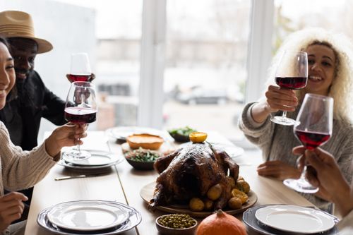 Free Glad diverse adult friends sitting at table with tasty dishes and toasting with glasses of wine during celebration of Thanksgiving Day Stock Photo